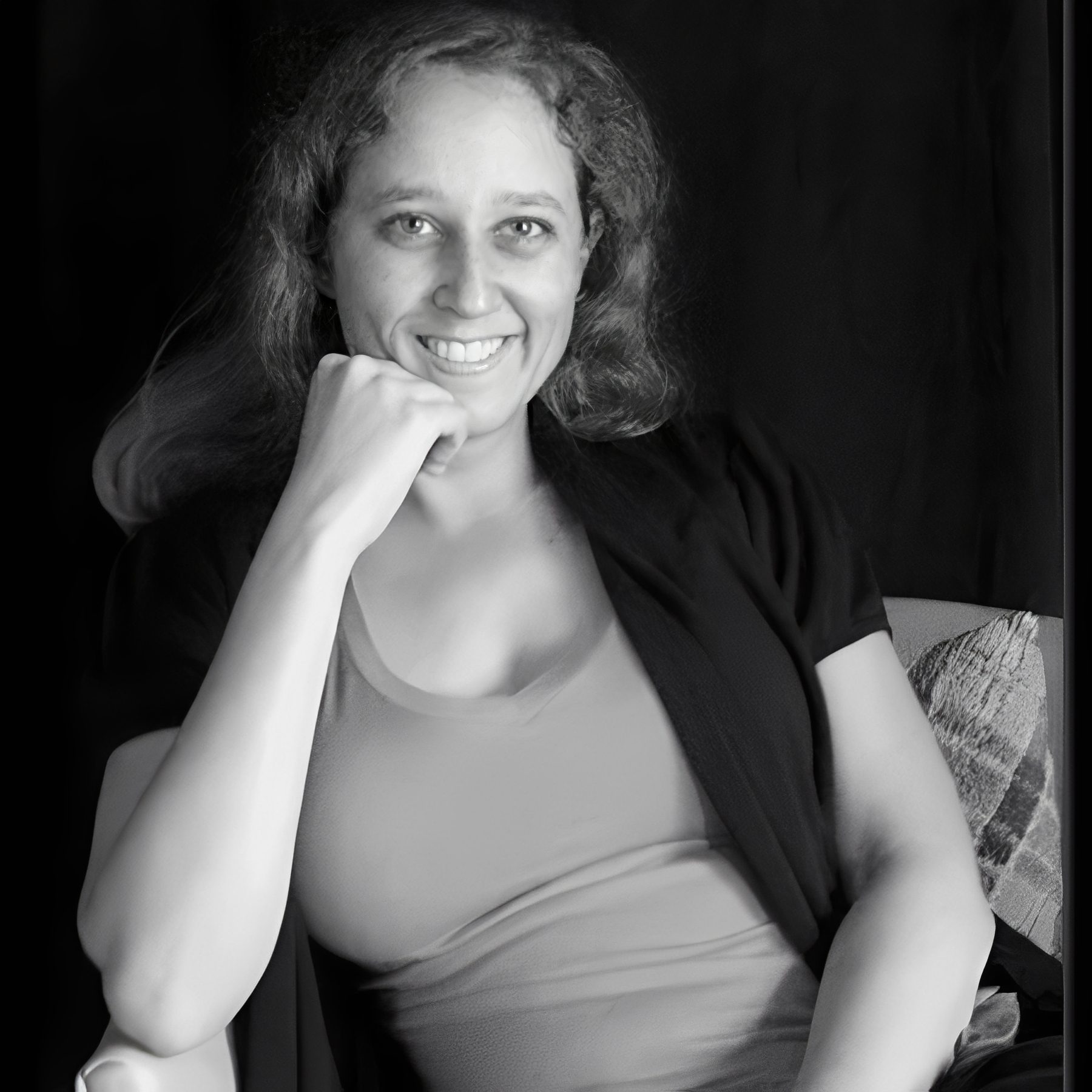 Smiling woman seated, hand resting on chin